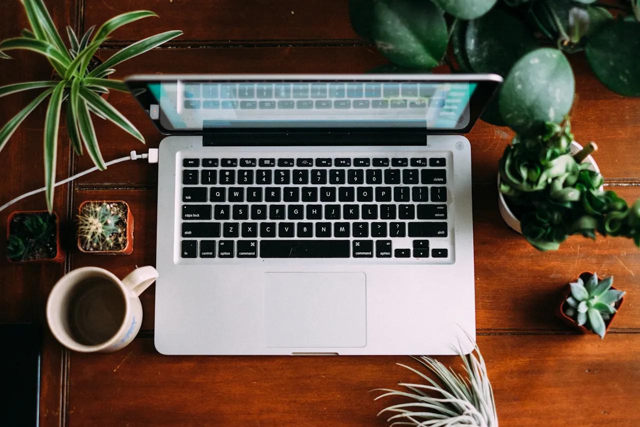 Laptop on wooden table with plants and coffee cup