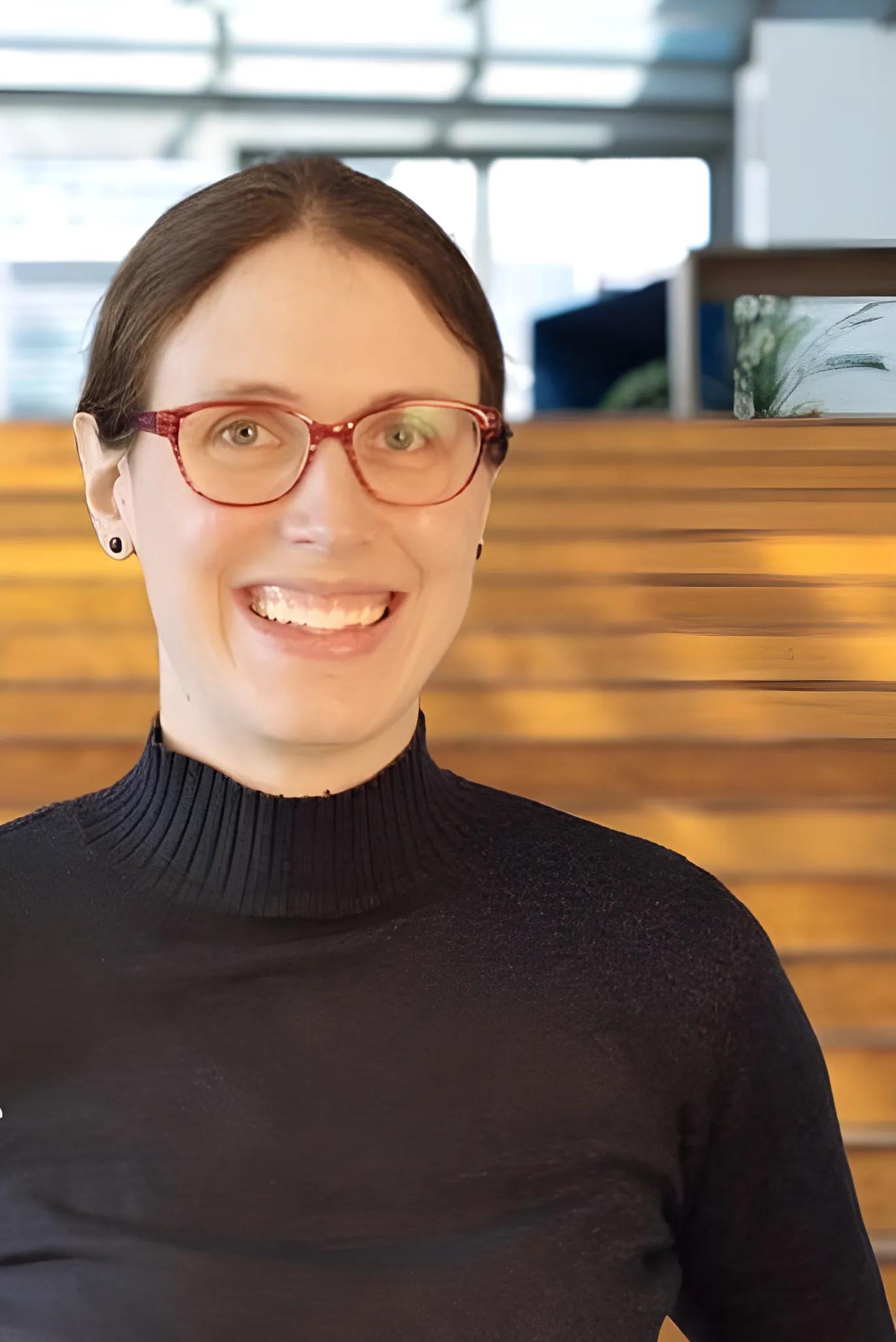 Portrait of a smiling person wearing glasses and a black sweater.