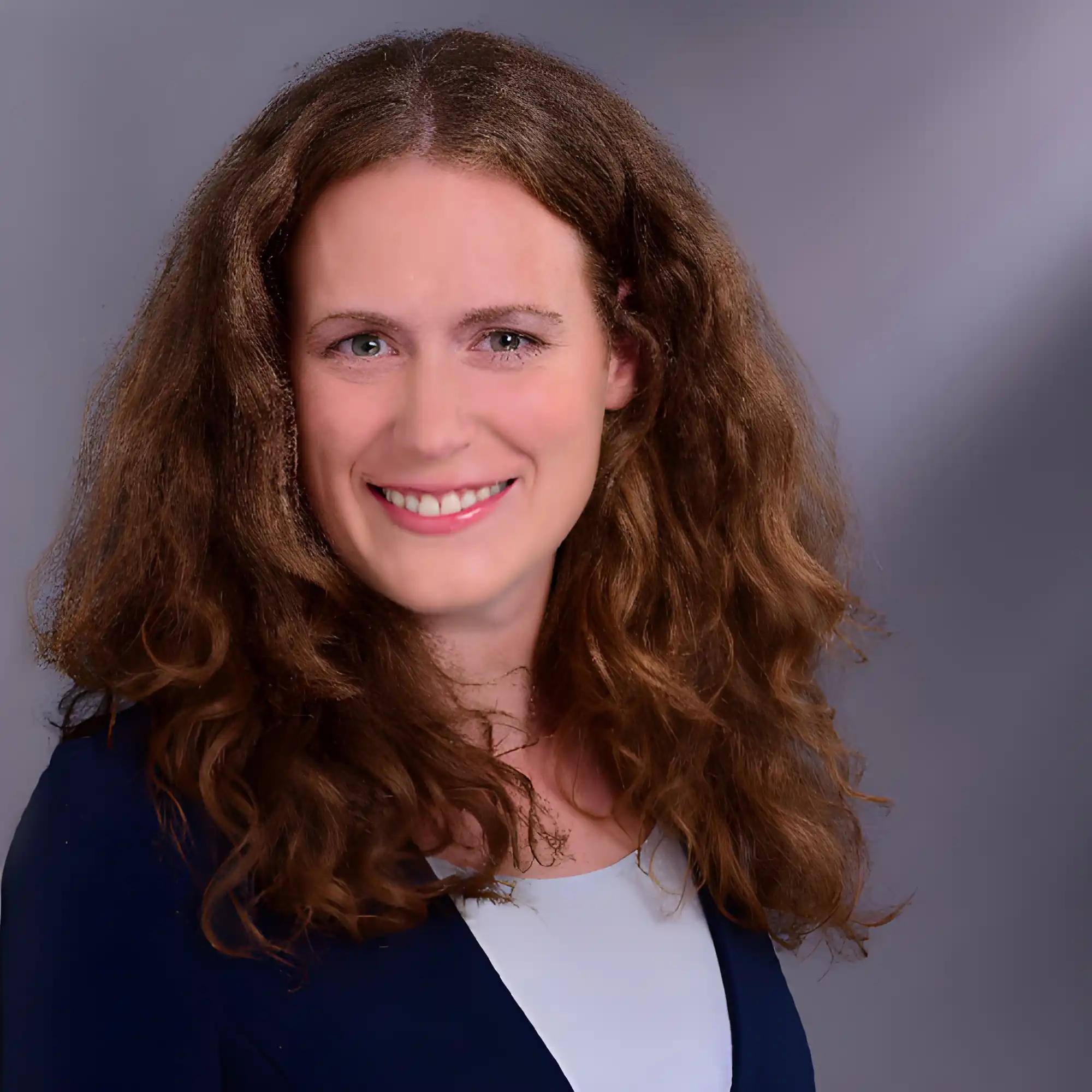Portrait of a smiling woman with long curly hair against a gray background