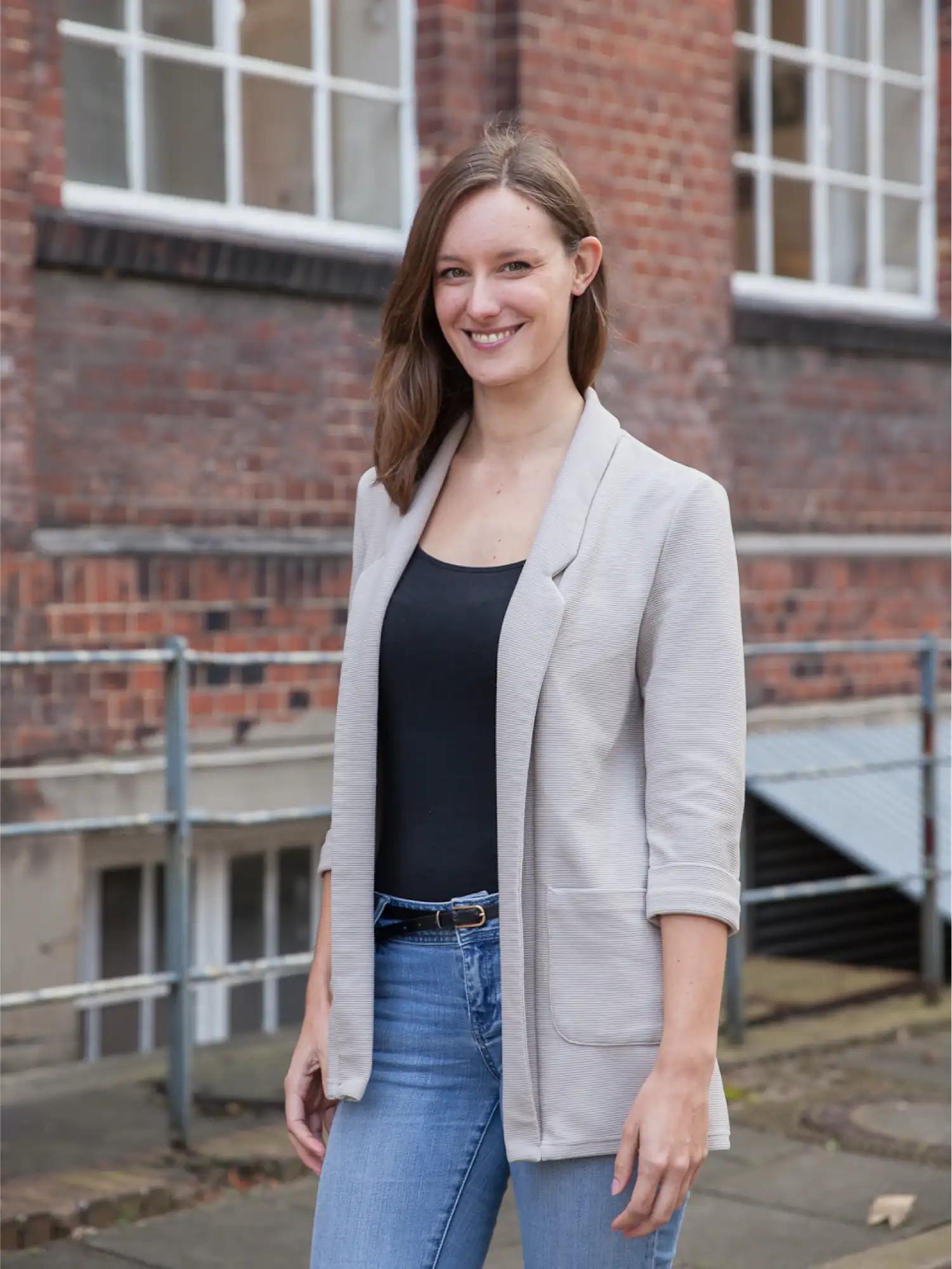 Woman in gray blazer in front of brick wall