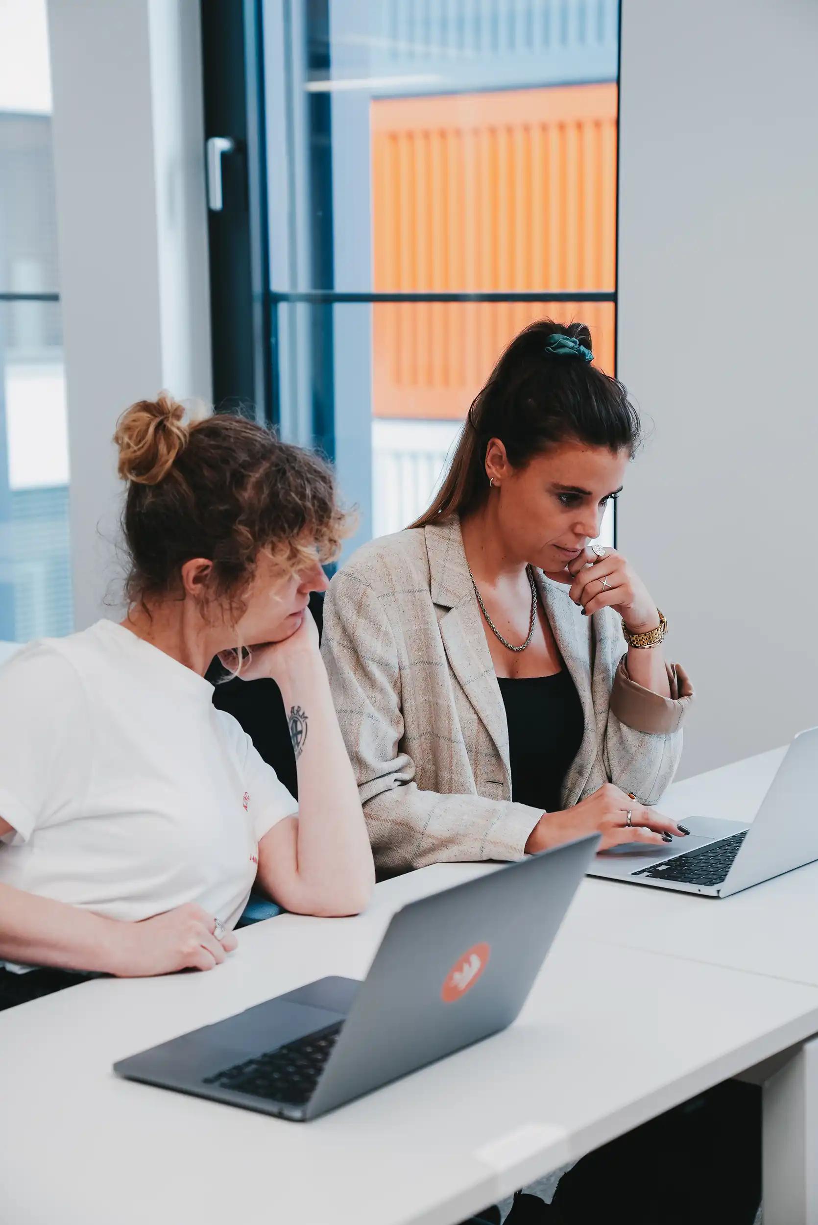 Zwei Frauen, die zusammen an Laptops in einem Büro arbeiten.
