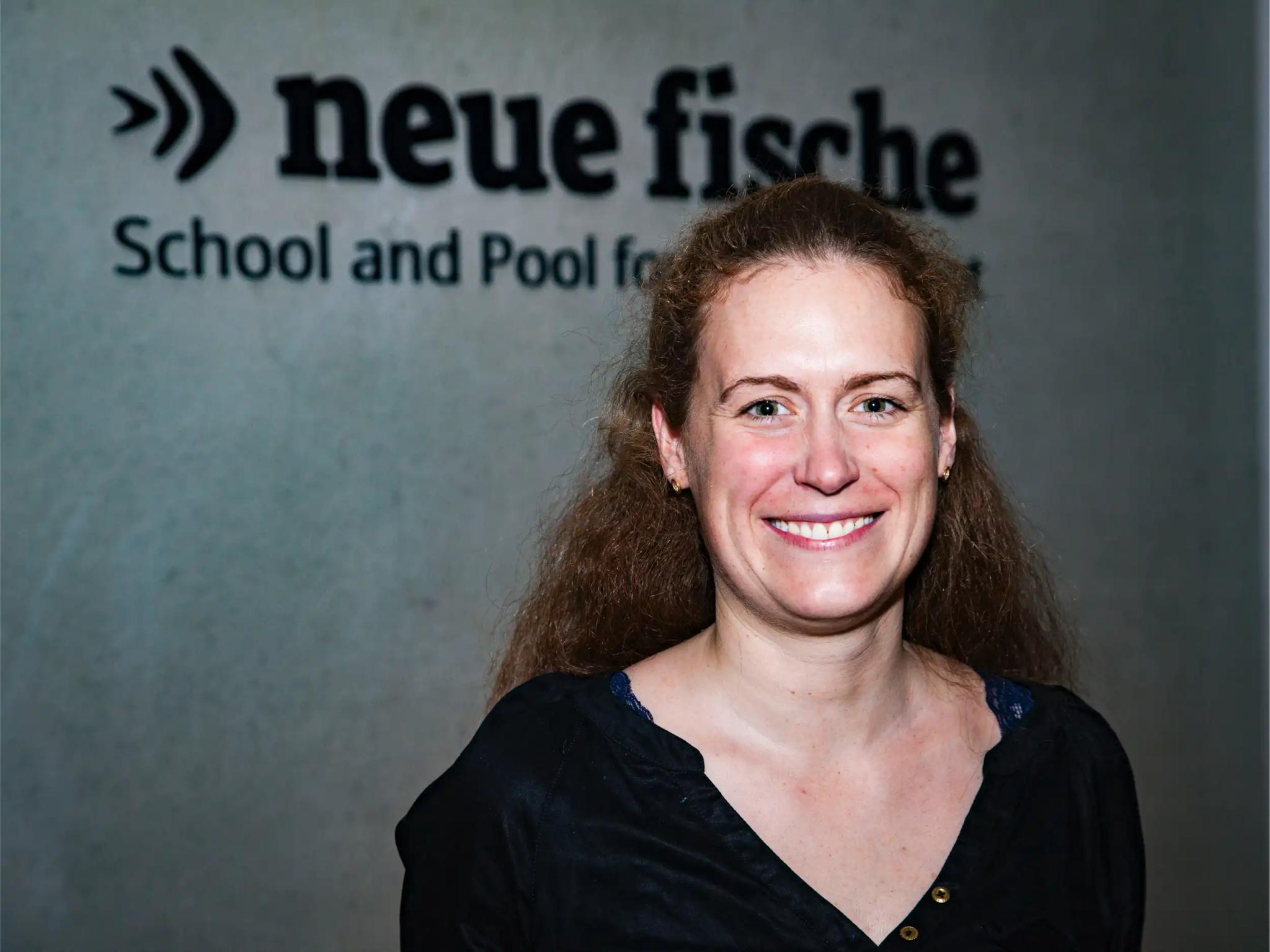 Portrait of a smiling woman in front of a wall with the text 'neue fische'.