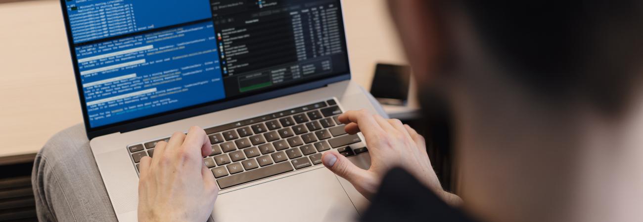Person typing on a laptop displaying code on the screen.