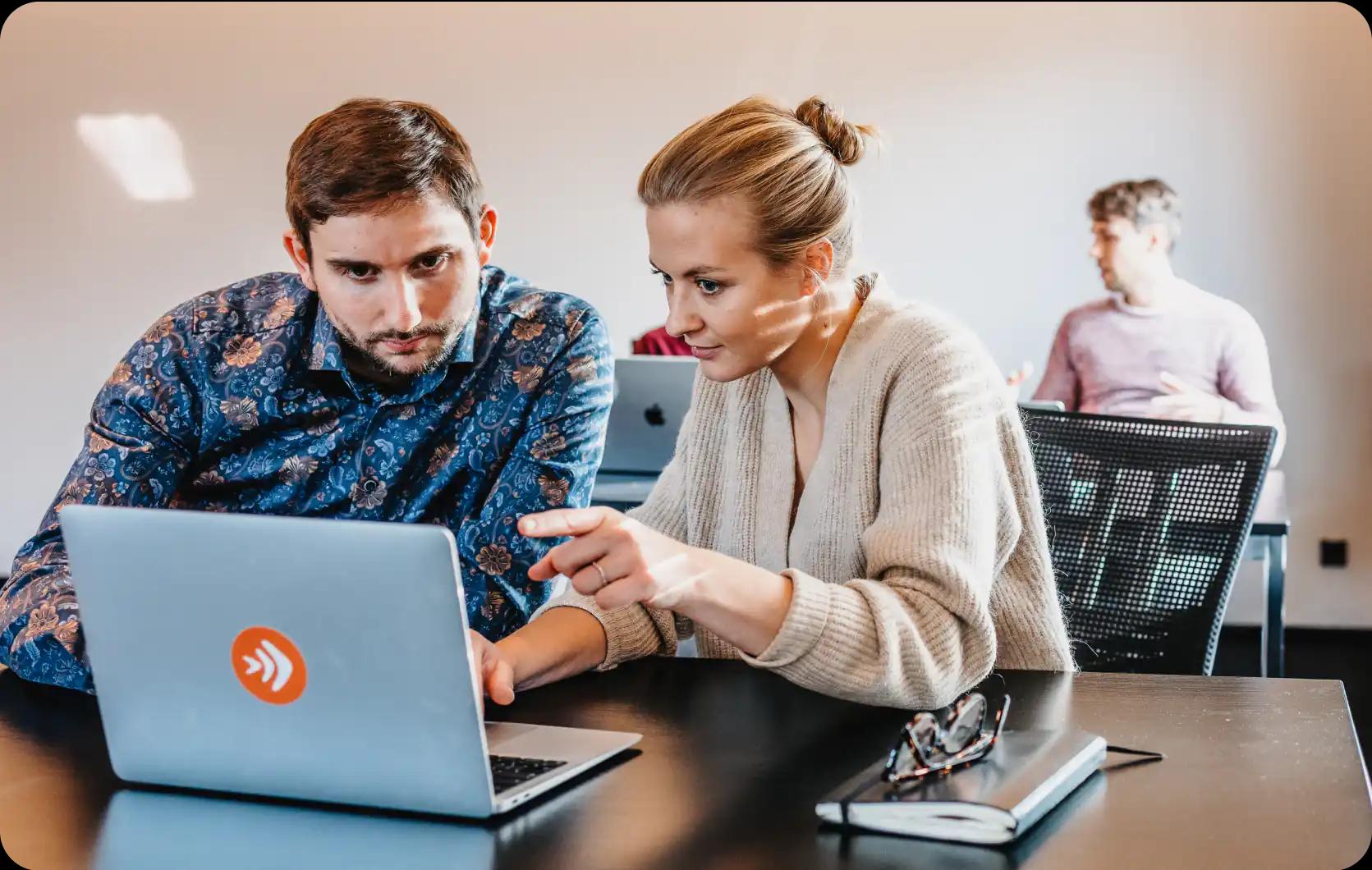 Two people working together on a laptop in an office.