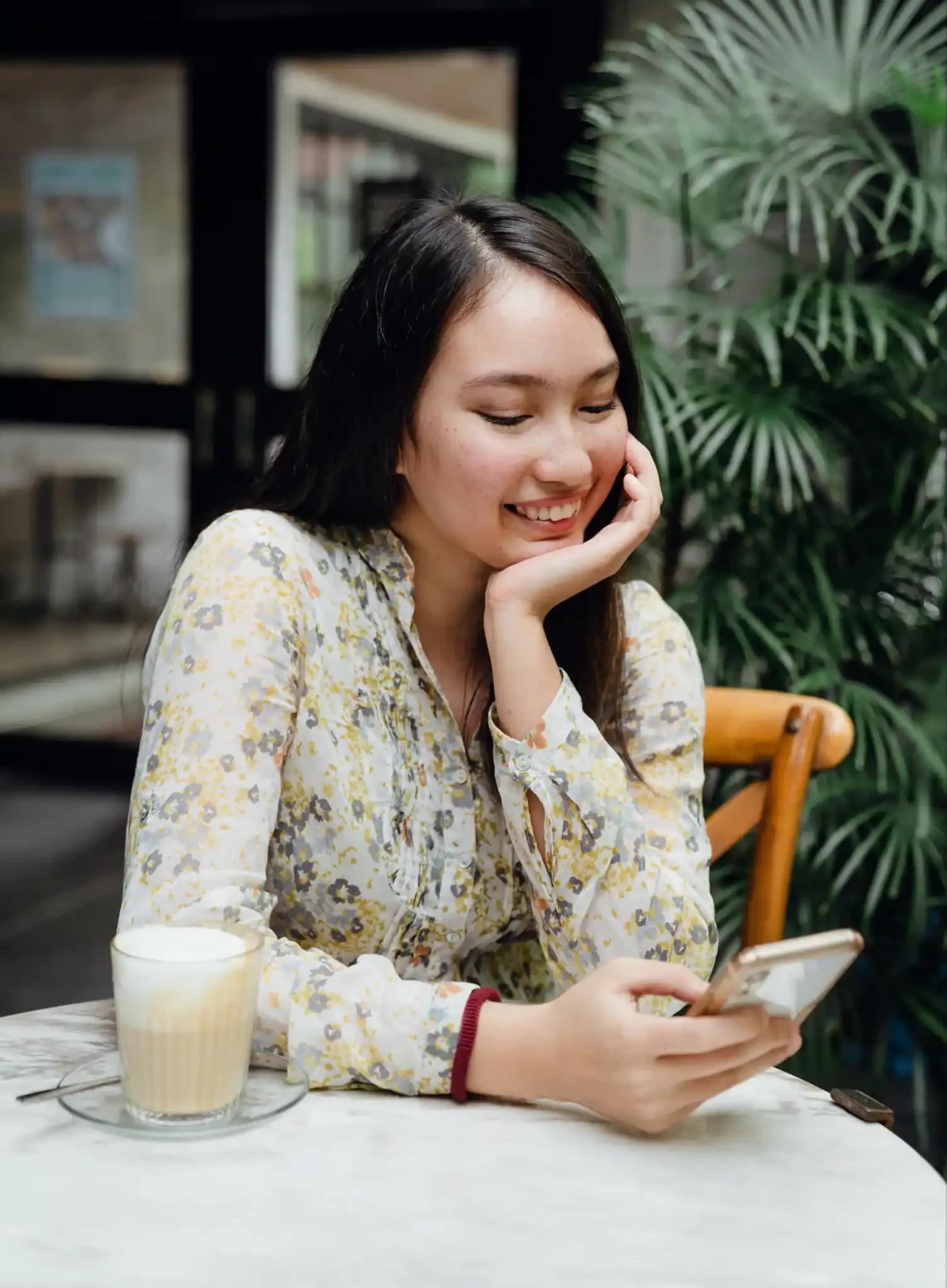 Junge Frau, die lächelnd auf ihr Handy schaut, während sie in einem Café sitzt.