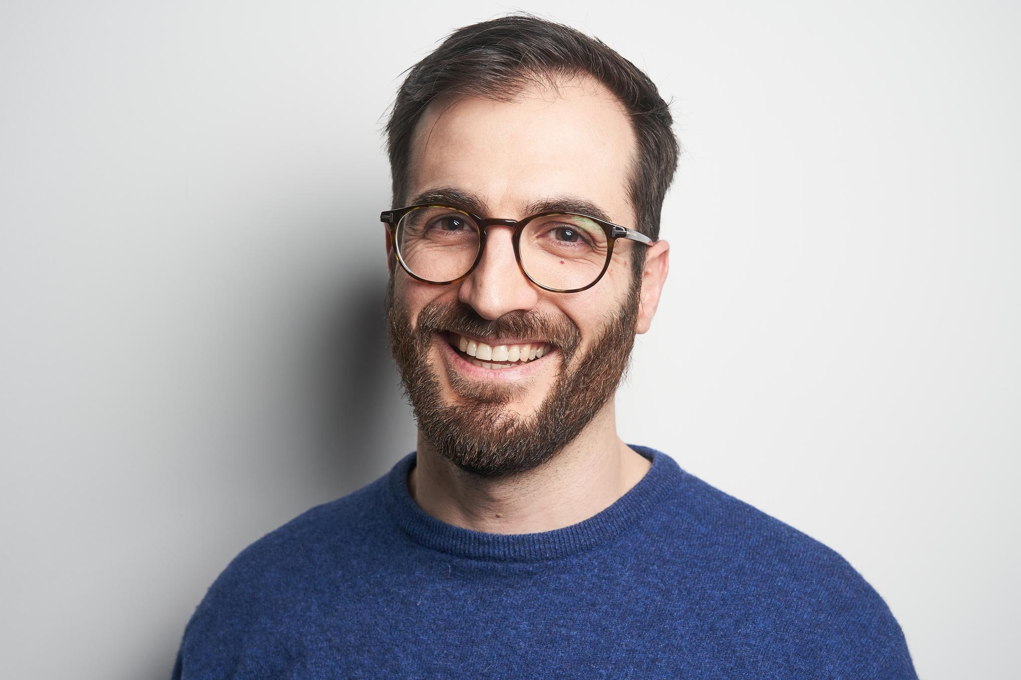 Mann mit Brille und blauem Pullover lächelt