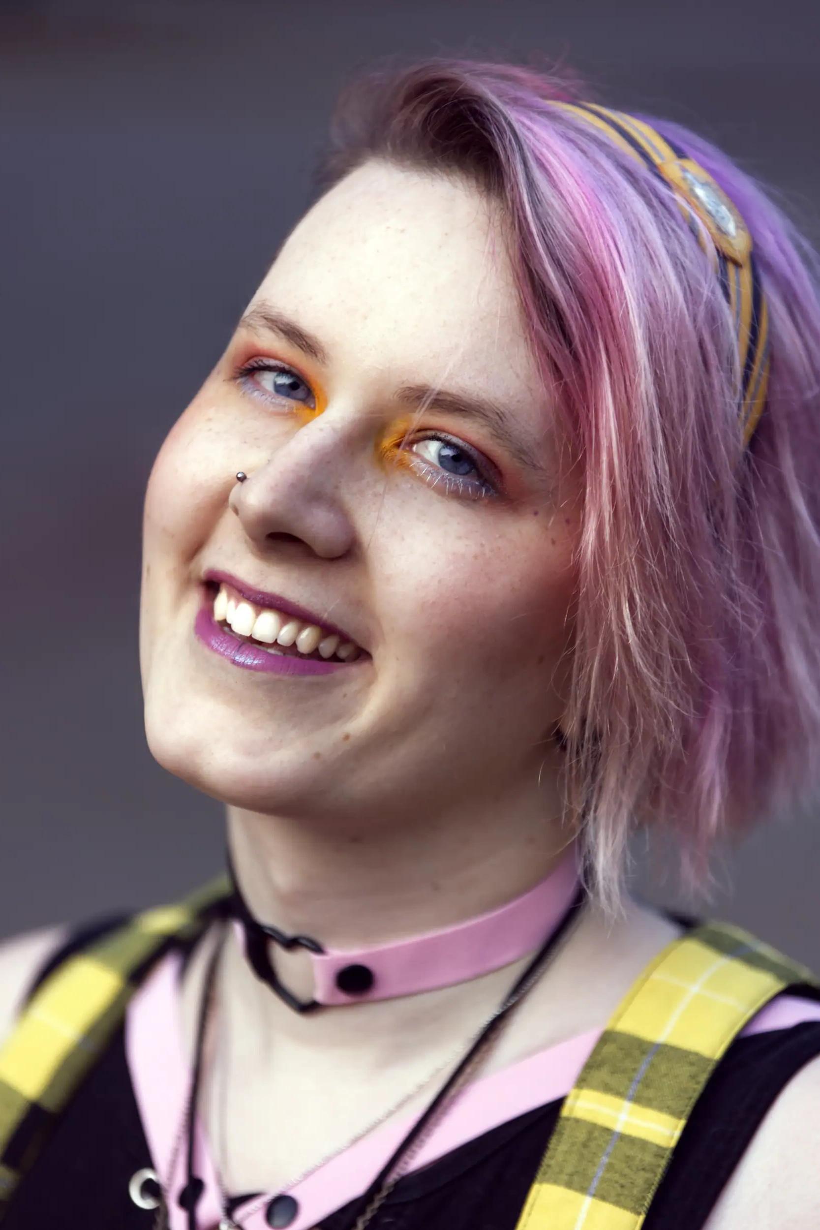 Portrait of a smiling young person with pink hair and yellow headband.
