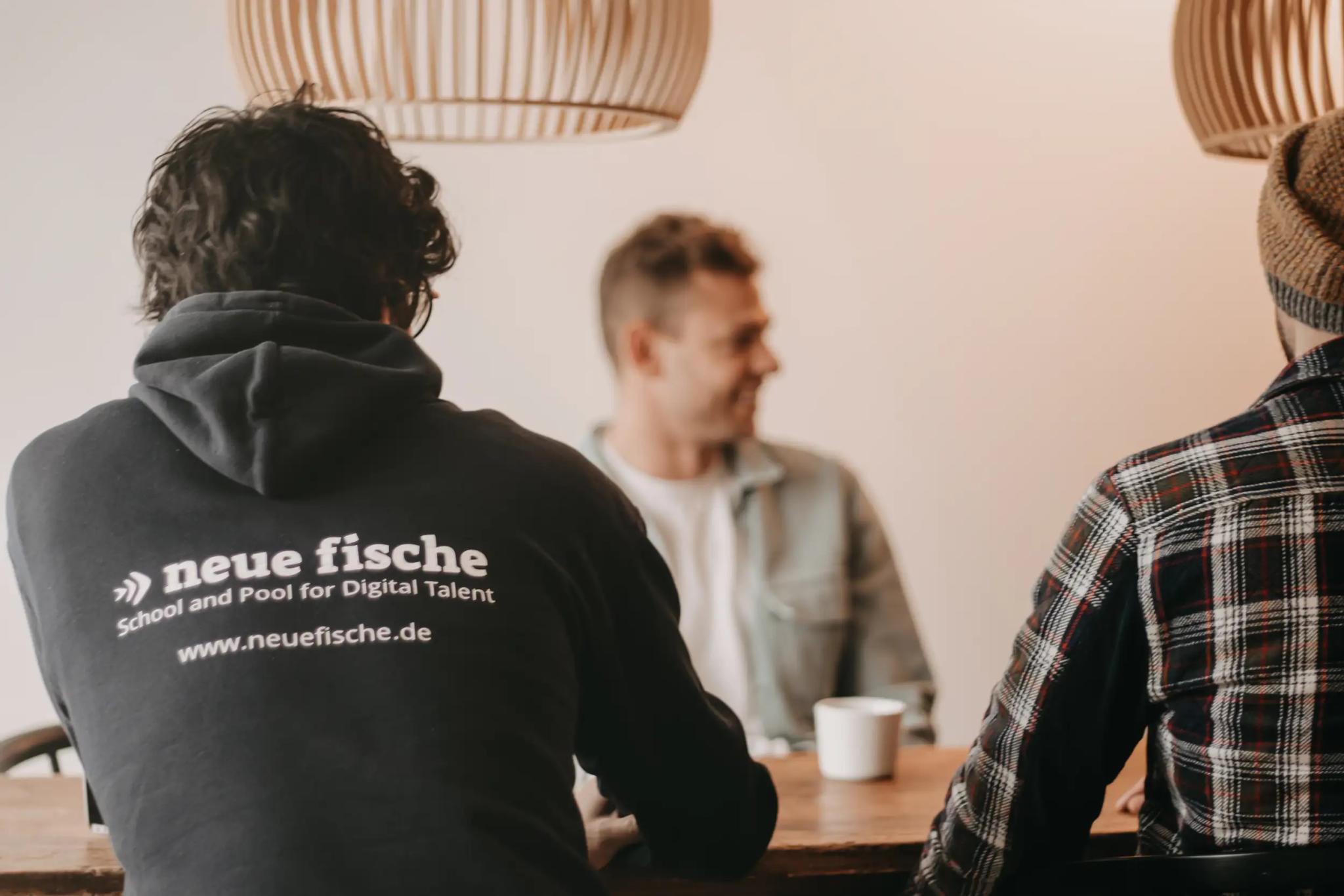 Drei Personen sitzen an einem Tisch im Gespräch.