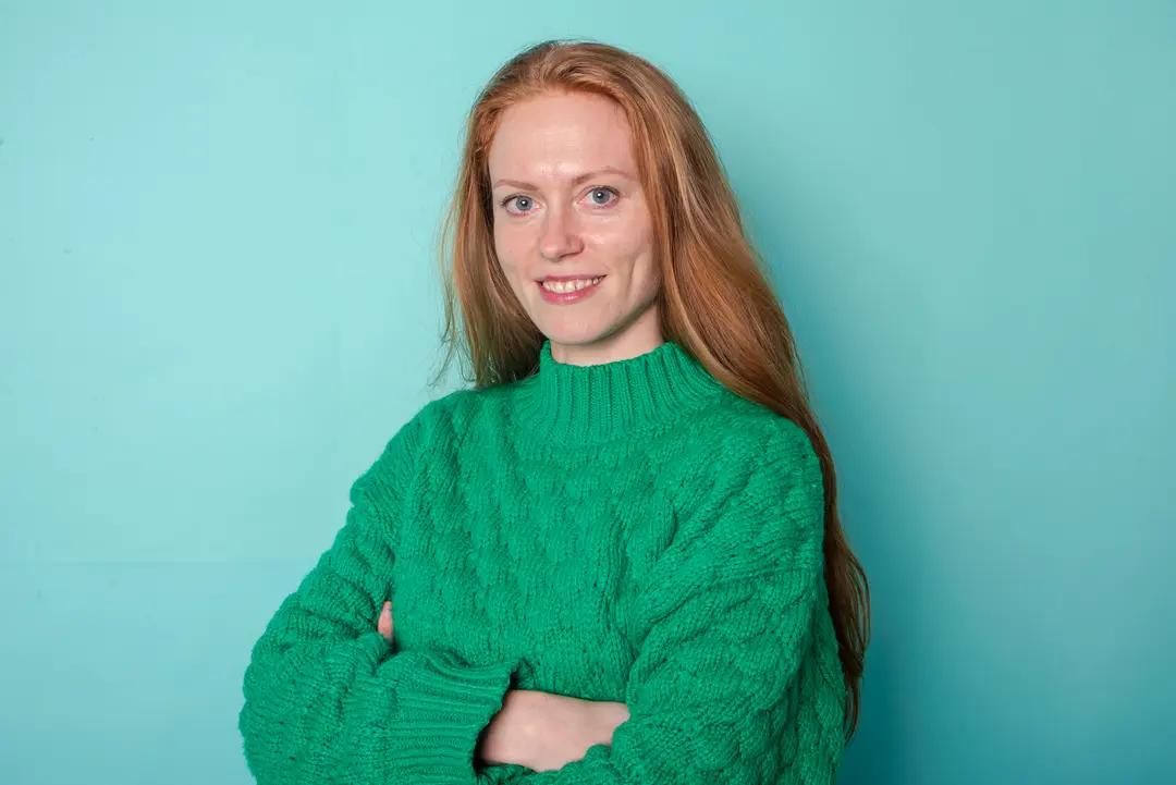 Frau mit grünem Pullover vor blauem Hintergrund.