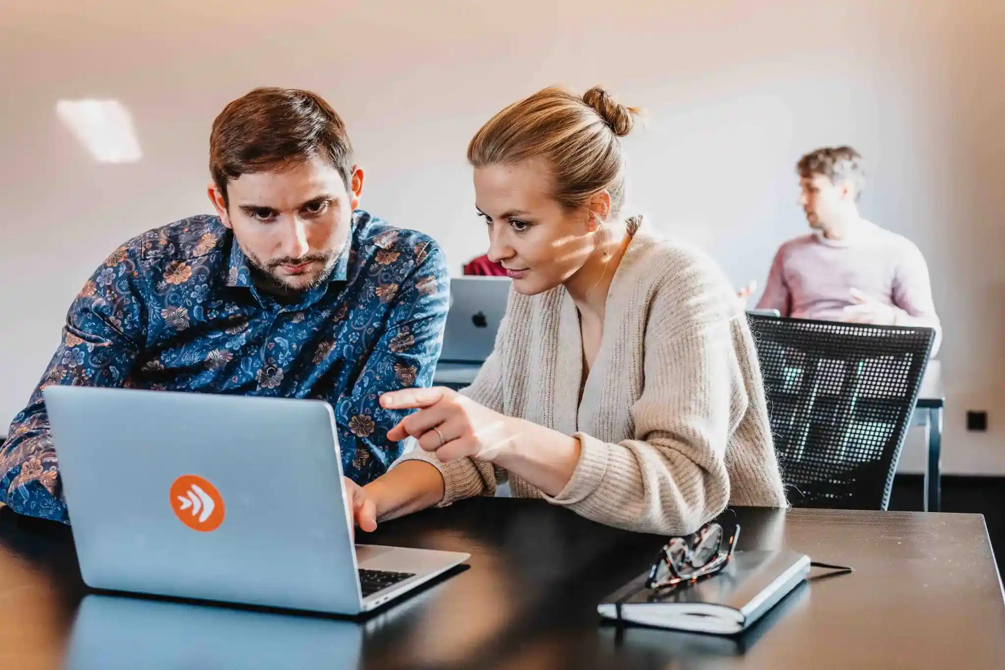 Two people working together on a laptop in an office.