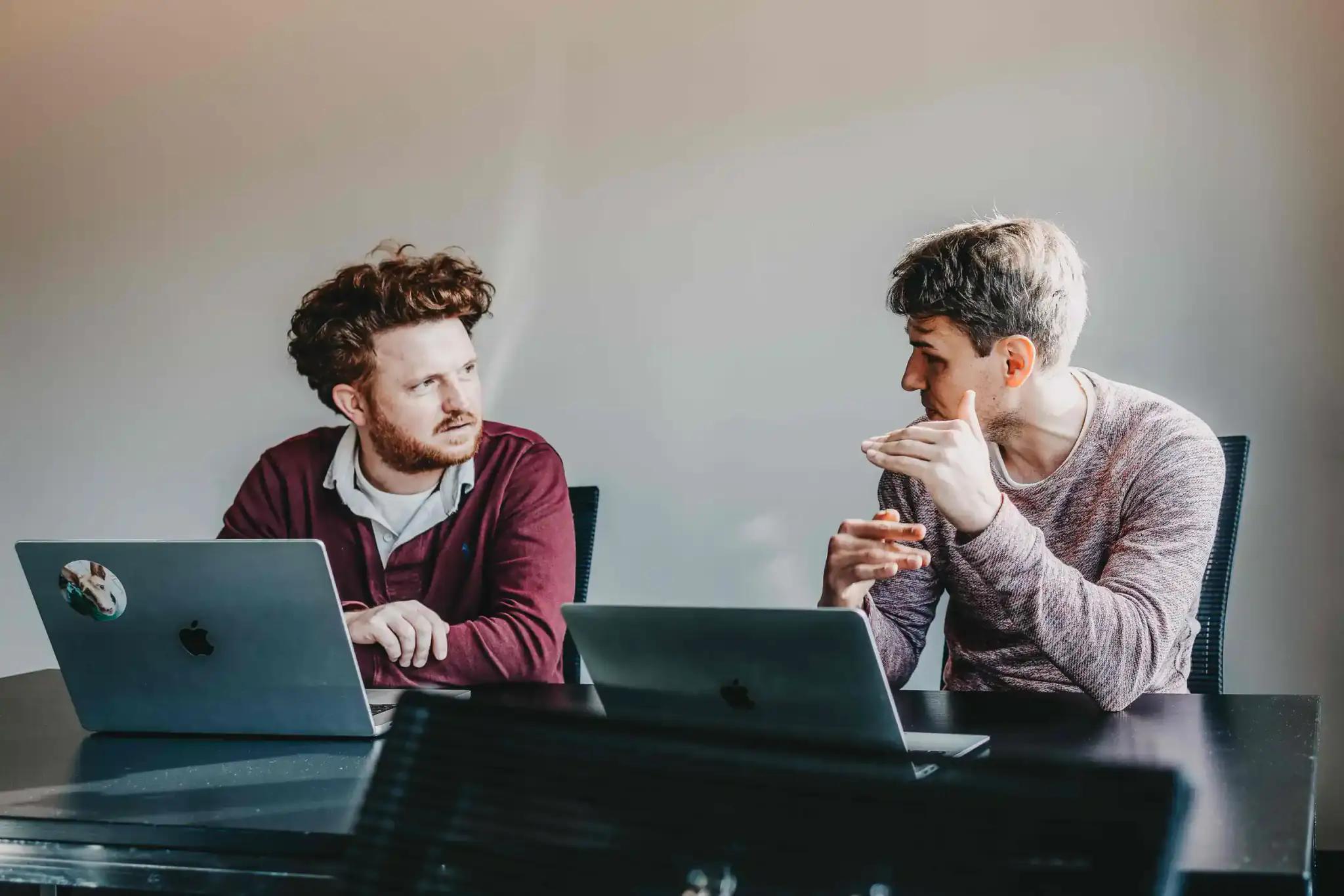 Zwei Männer diskutieren bei der Arbeit mit Laptops.