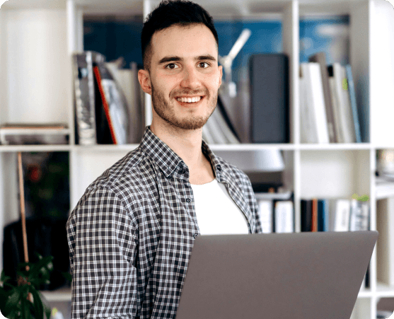 Junger Mann mit Laptop vor Bücherregal
