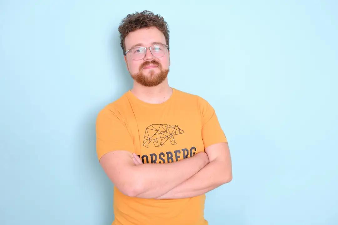 Mann mit Brille und orangefarbenem T-Shirt vor blauem Hintergrund