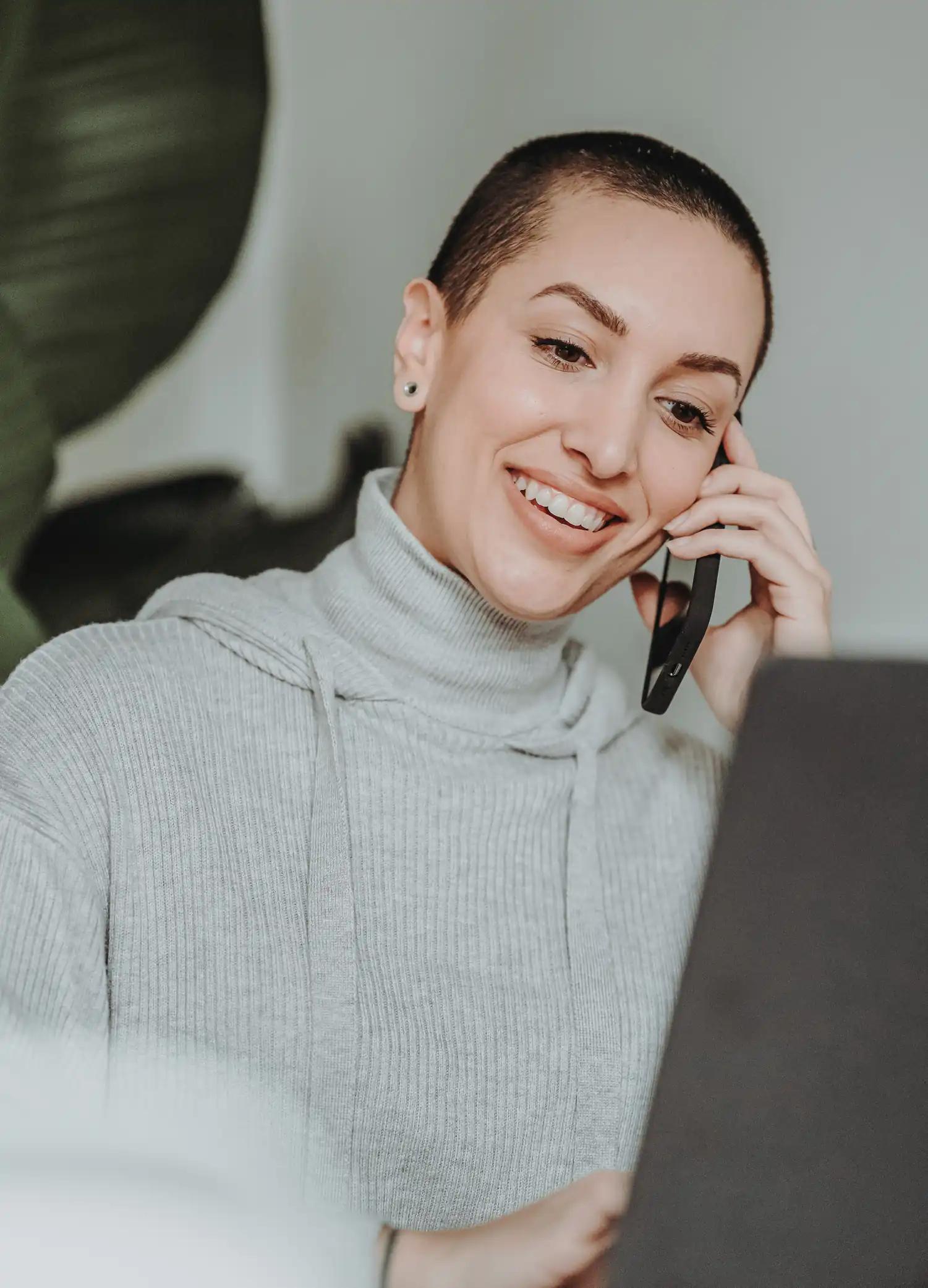 Frau spricht lächelnd am Telefon und arbeitet am Laptop.