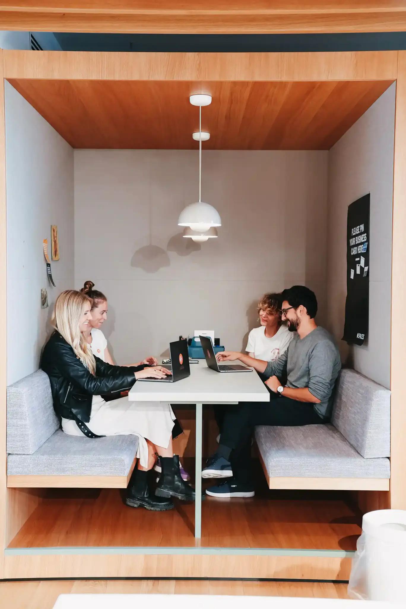 Vier Personen arbeiten zusammen an Laptops in einer modernen Meeting-Nische.