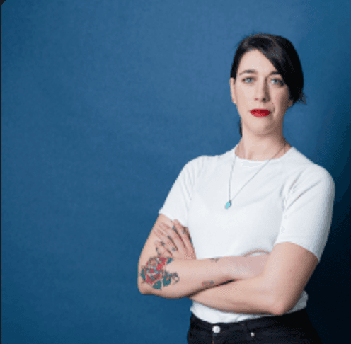 Frau mit weißen T-Shirt und tätowiertem Arm vor blauem Hintergrund.