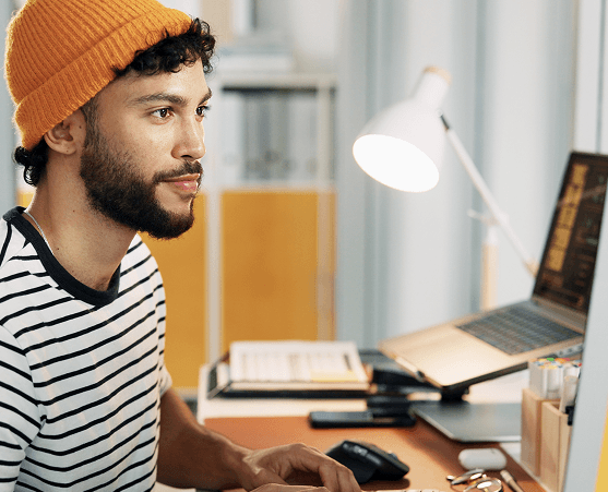 Mann mit orangener Mütze arbeitet am Computer