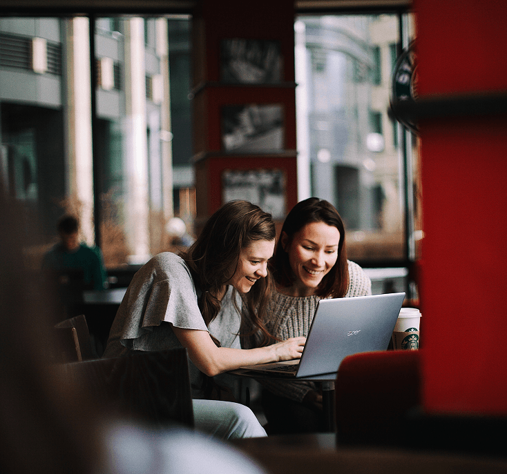 Two women working together on a laptop in a café.