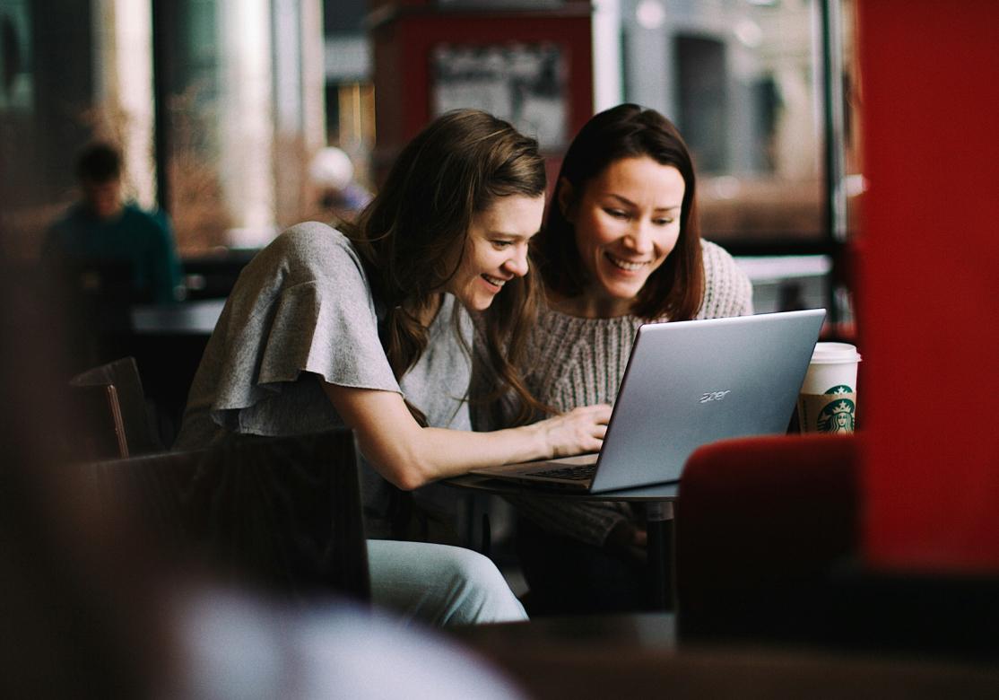 Zwei Frauen, die zusammen an einem Laptop arbeiten.