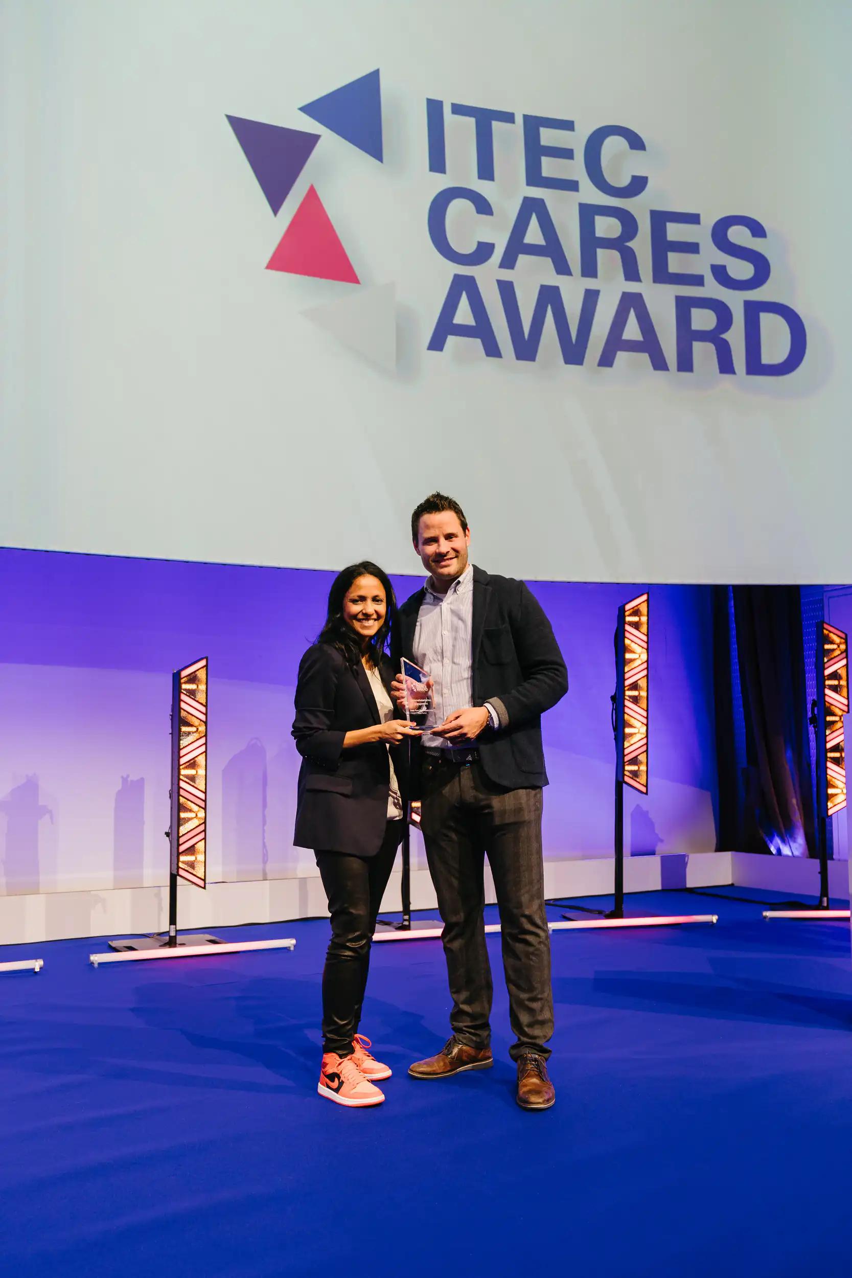 Zwei Personen halten eine Auszeichnung auf der Bühne der ITEC Cares Award Veranstaltung.