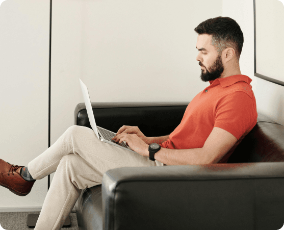 Mann sitzt auf einem Sofa und arbeitet an einem Laptop.
