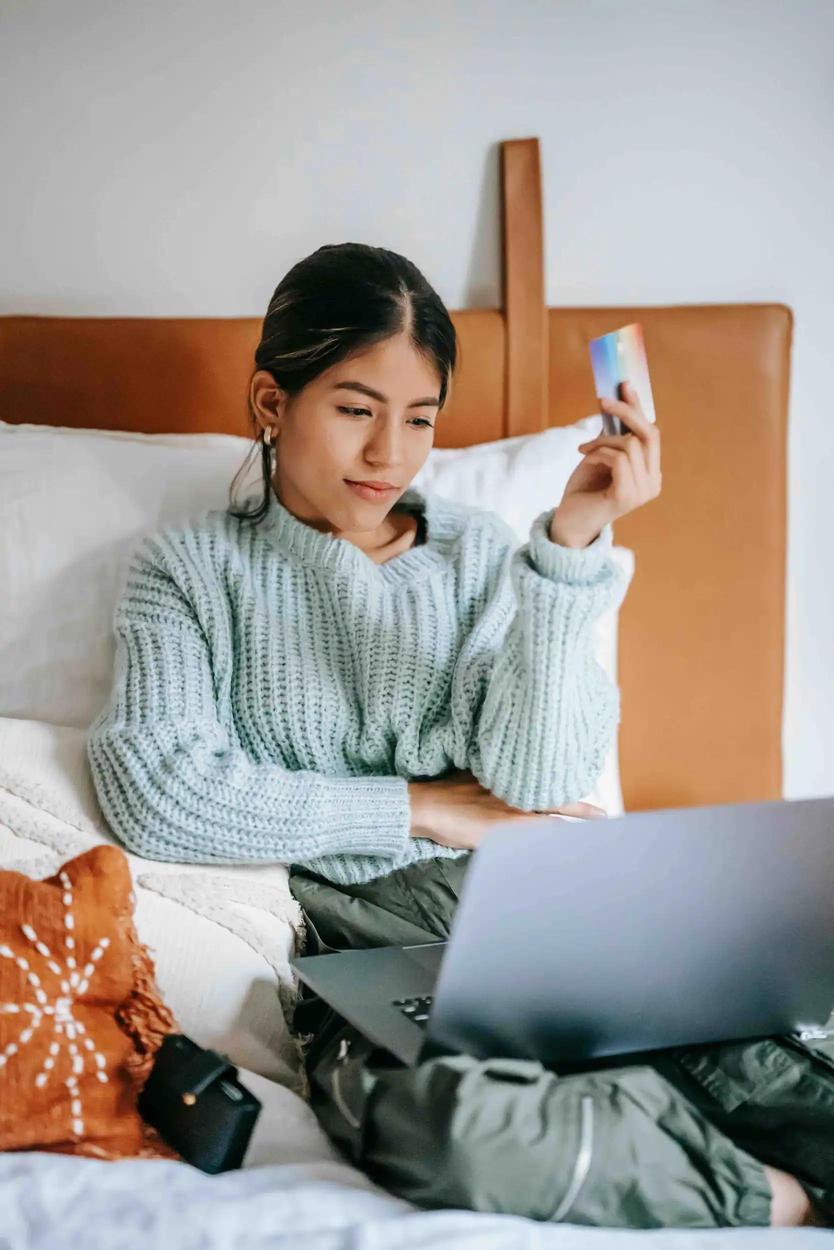 Woman sitting on bed with laptop holding a credit card