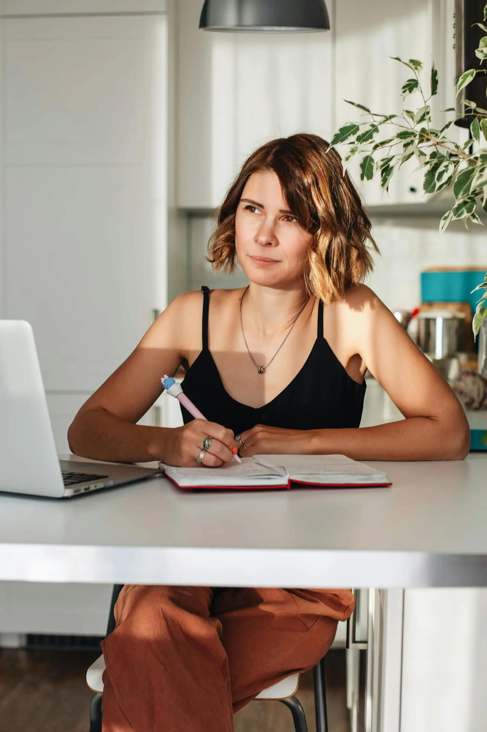Woman sitting at table with laptop and notebook.