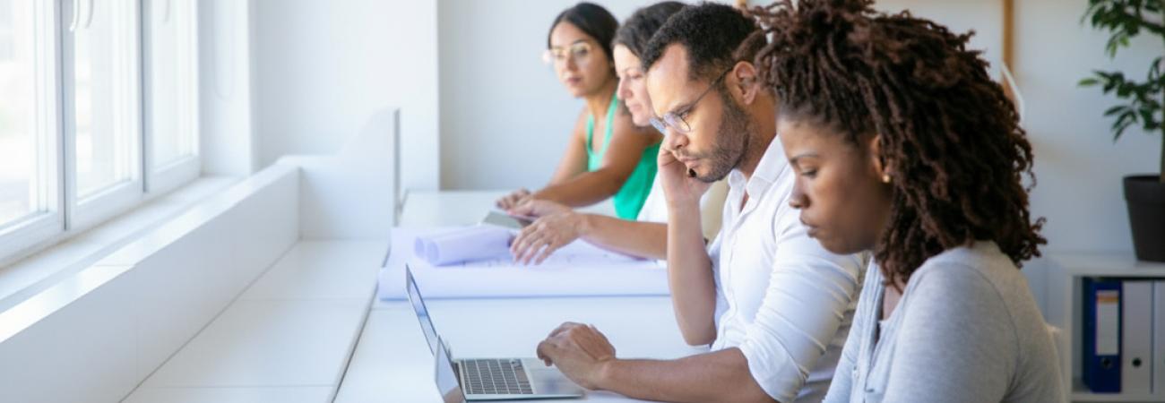 People working focused on laptops in a bright office.
