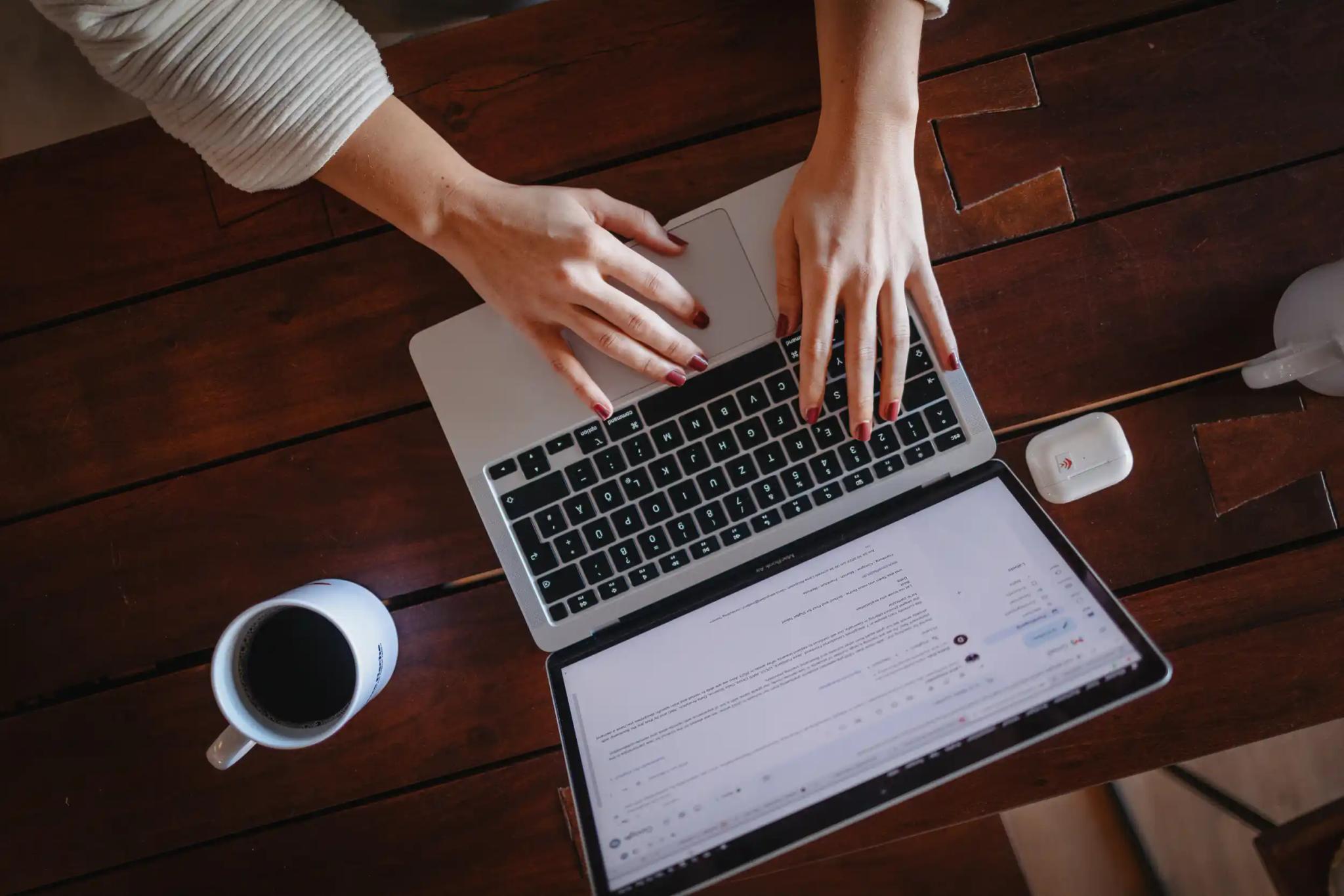 Person tippt auf Laptop-Tastatur am Holztisch mit Kaffee und Kopfhörern.