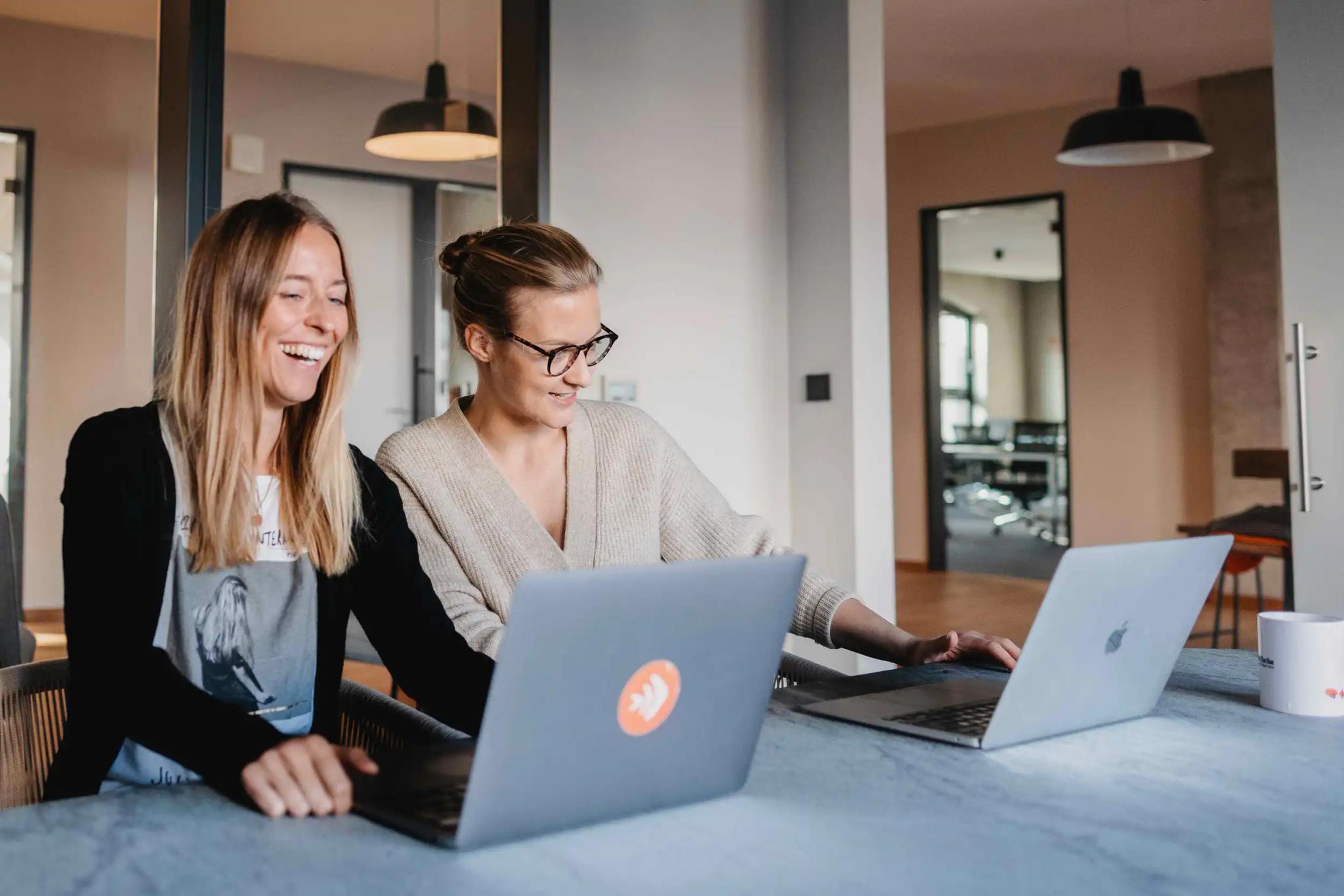 Two women working together on laptops in an office.