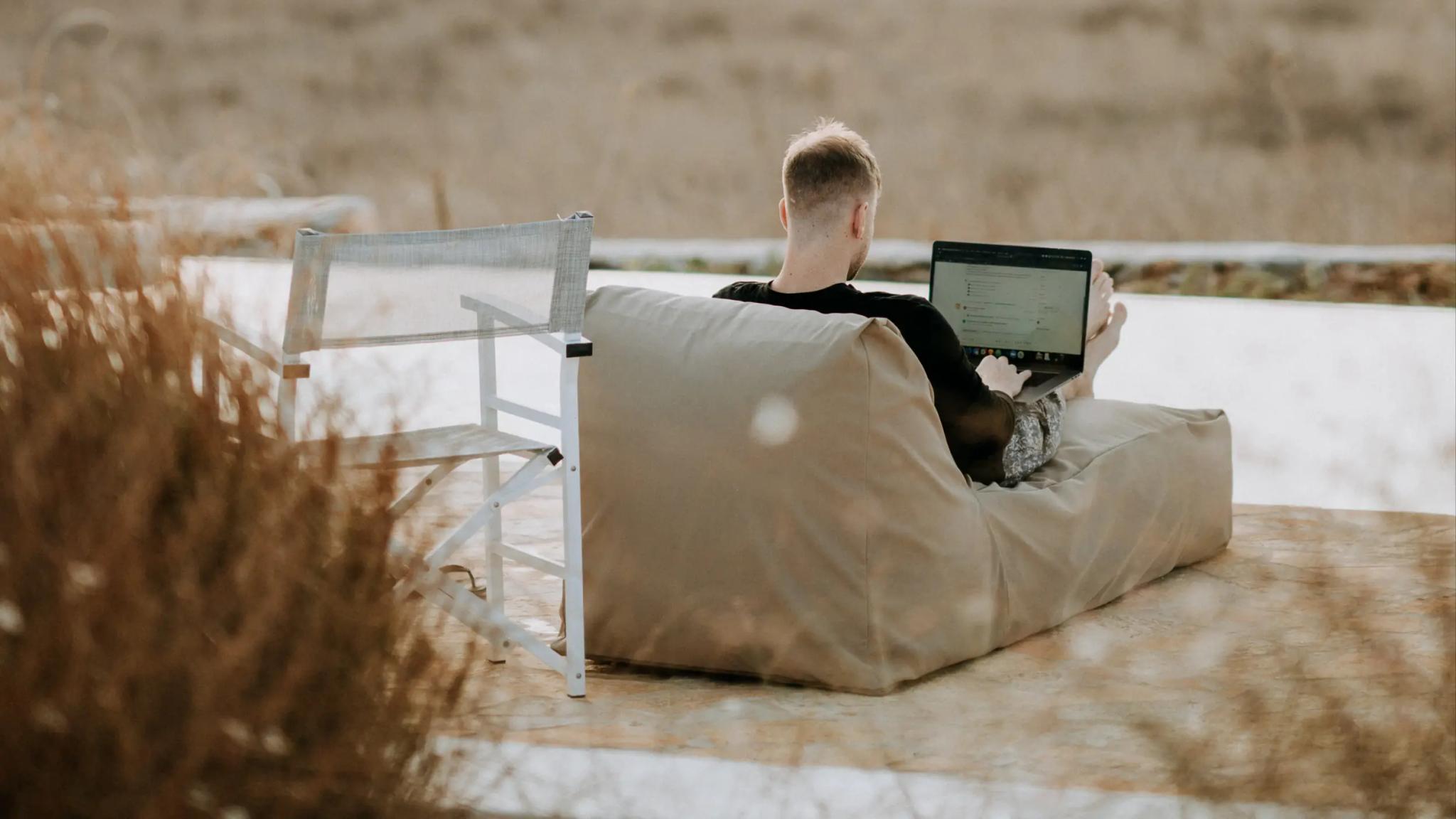 Person sitting outdoors on a couch working on a laptop.