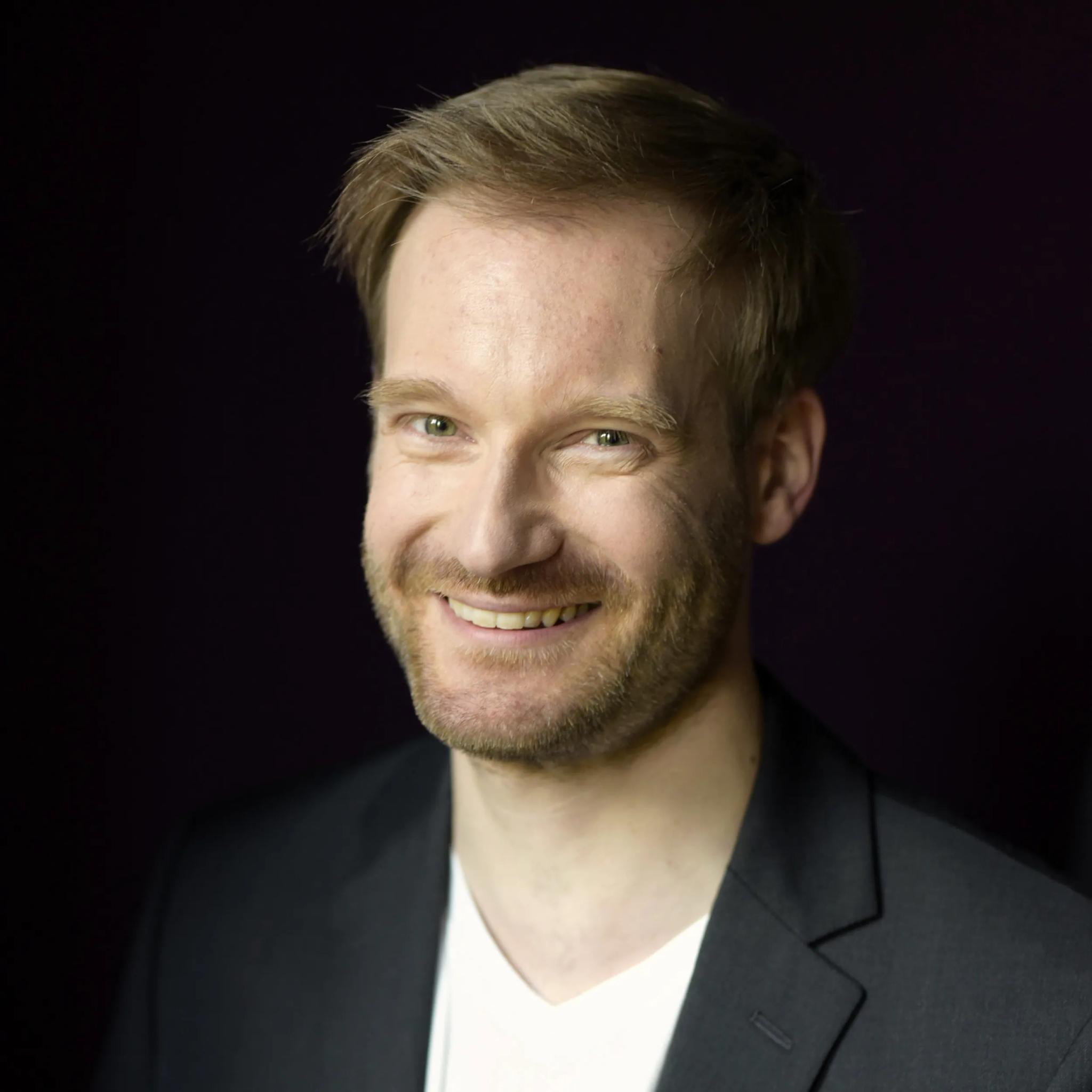 Porträt eines lächelnden Mannes in dunklem Anzug vor dunklem Hintergrund