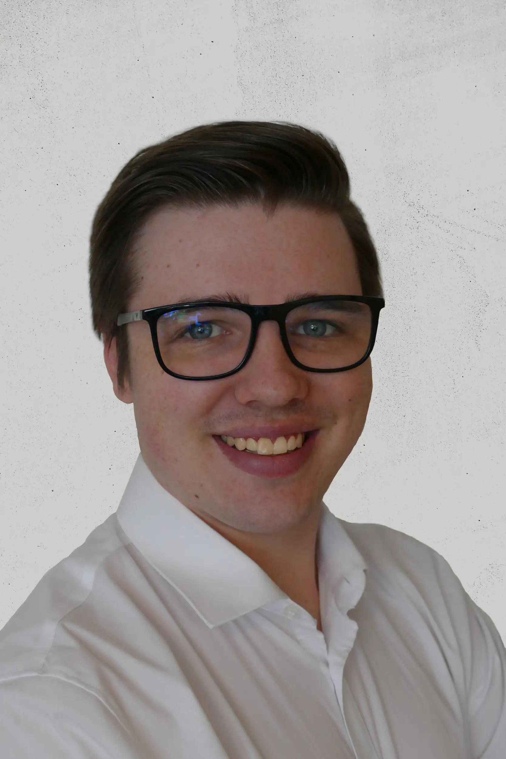 Porträt eines lächelnden Mannes mit Brille und weißem Hemd.