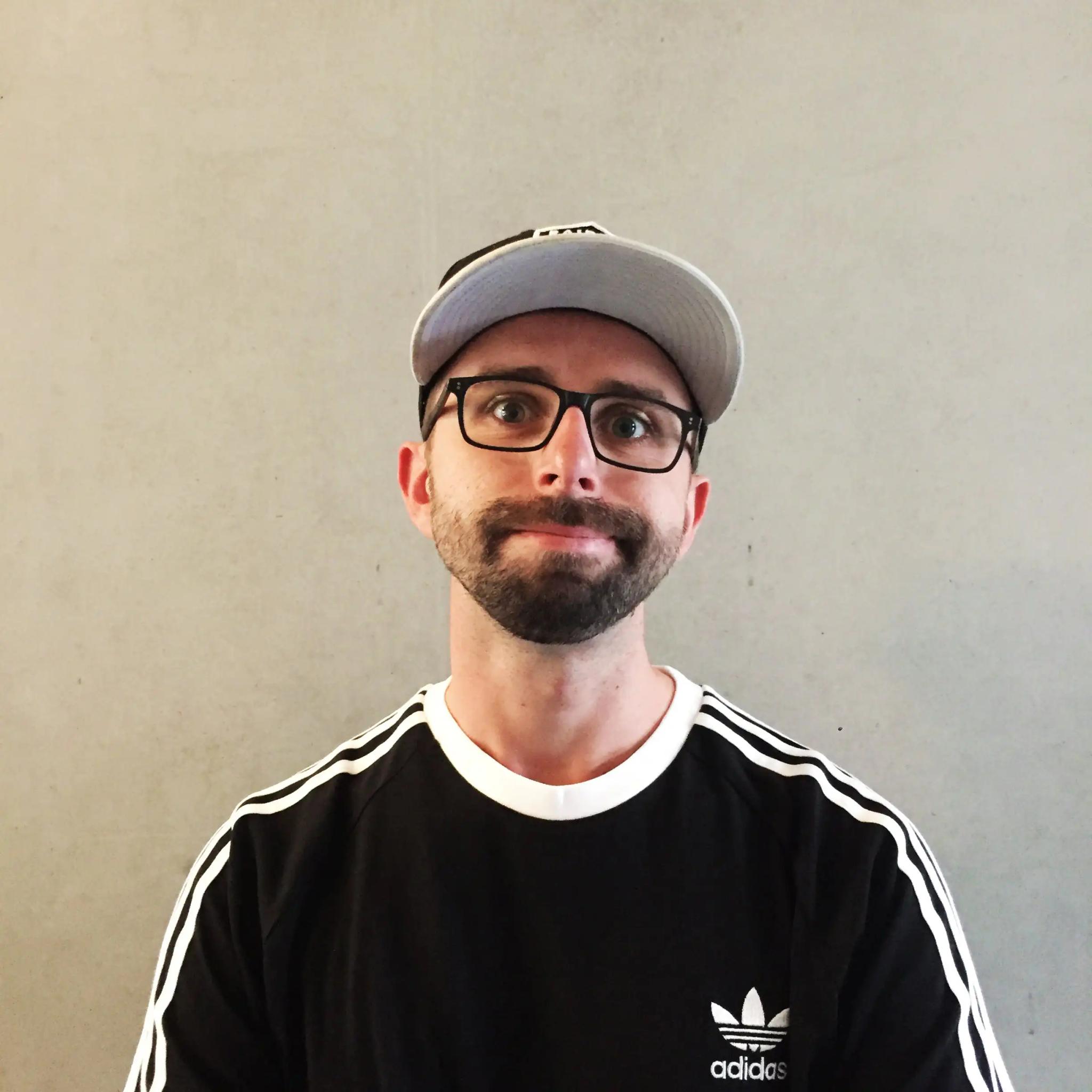 Portrait of a man with beard, glasses, and baseball cap against gray background