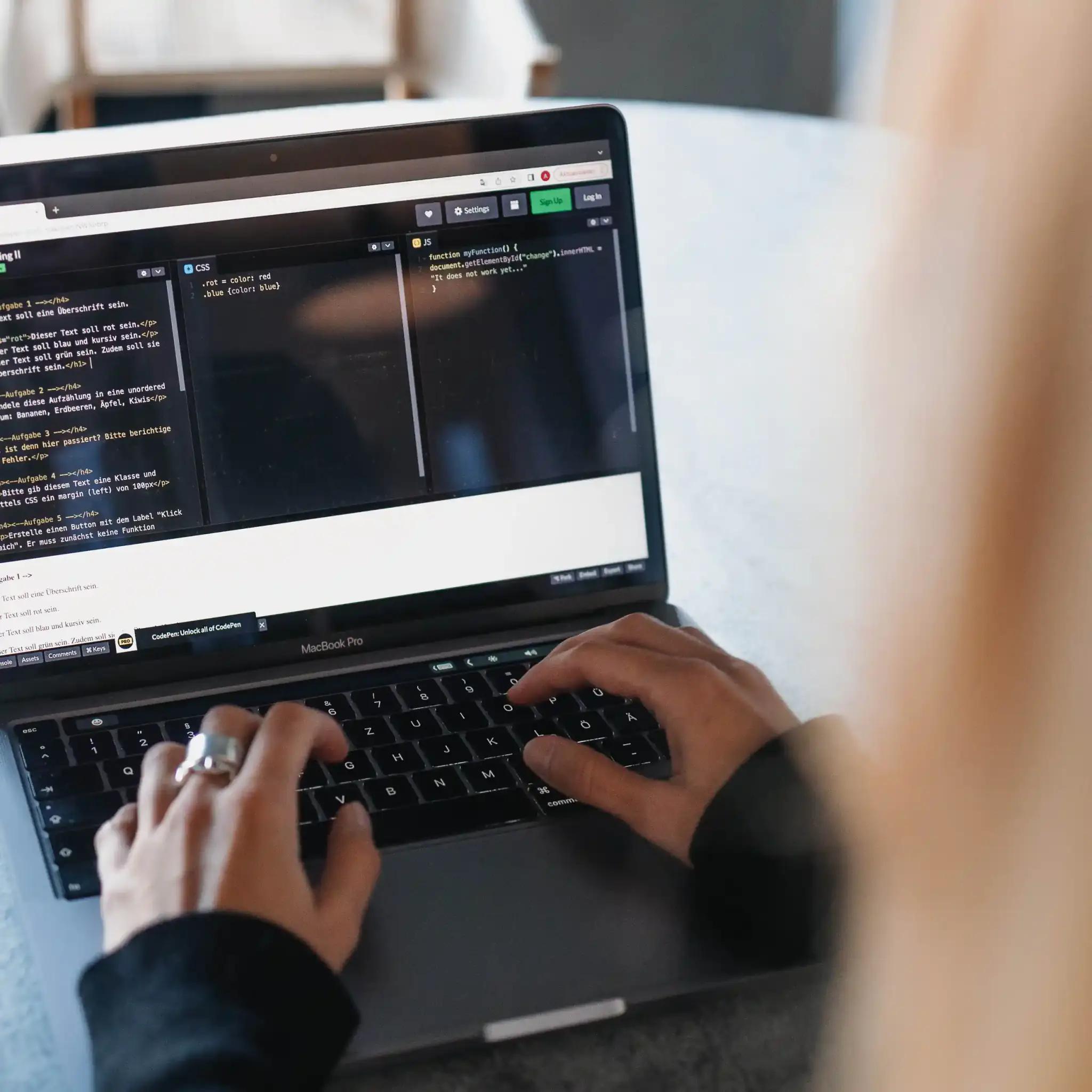 Person tippt auf einem Laptop mit Programmiercode auf dem Bildschirm.