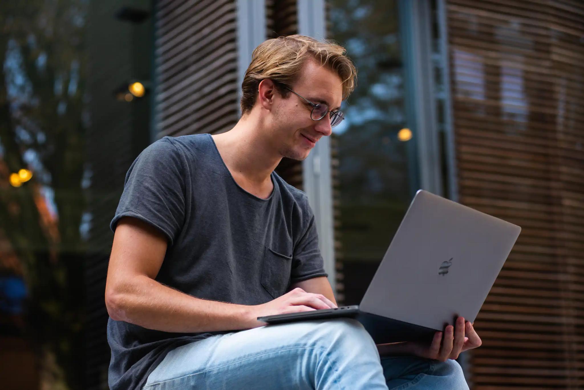 Junger Mann arbeitet an Laptop draußen.