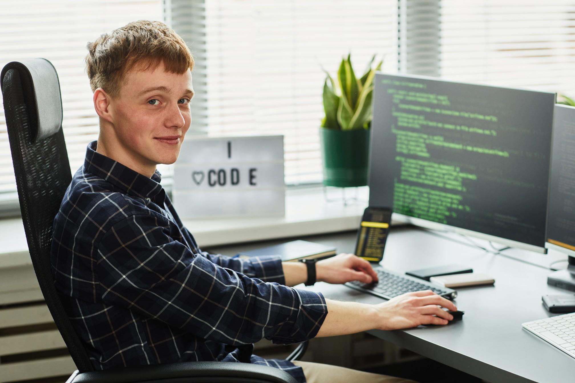 Junger Mann sitzt am Schreibtisch und programmiert am Computer.