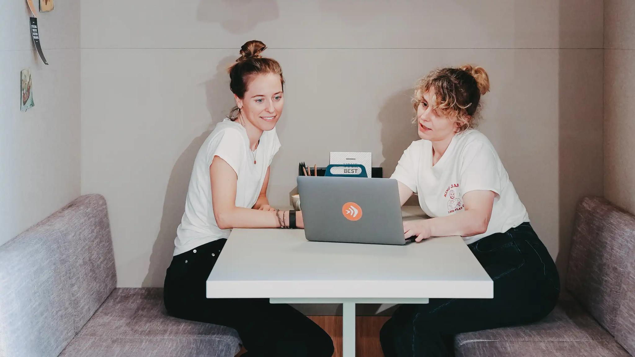 Zwei Frauen sitzen an einem Tisch mit einem Laptop.