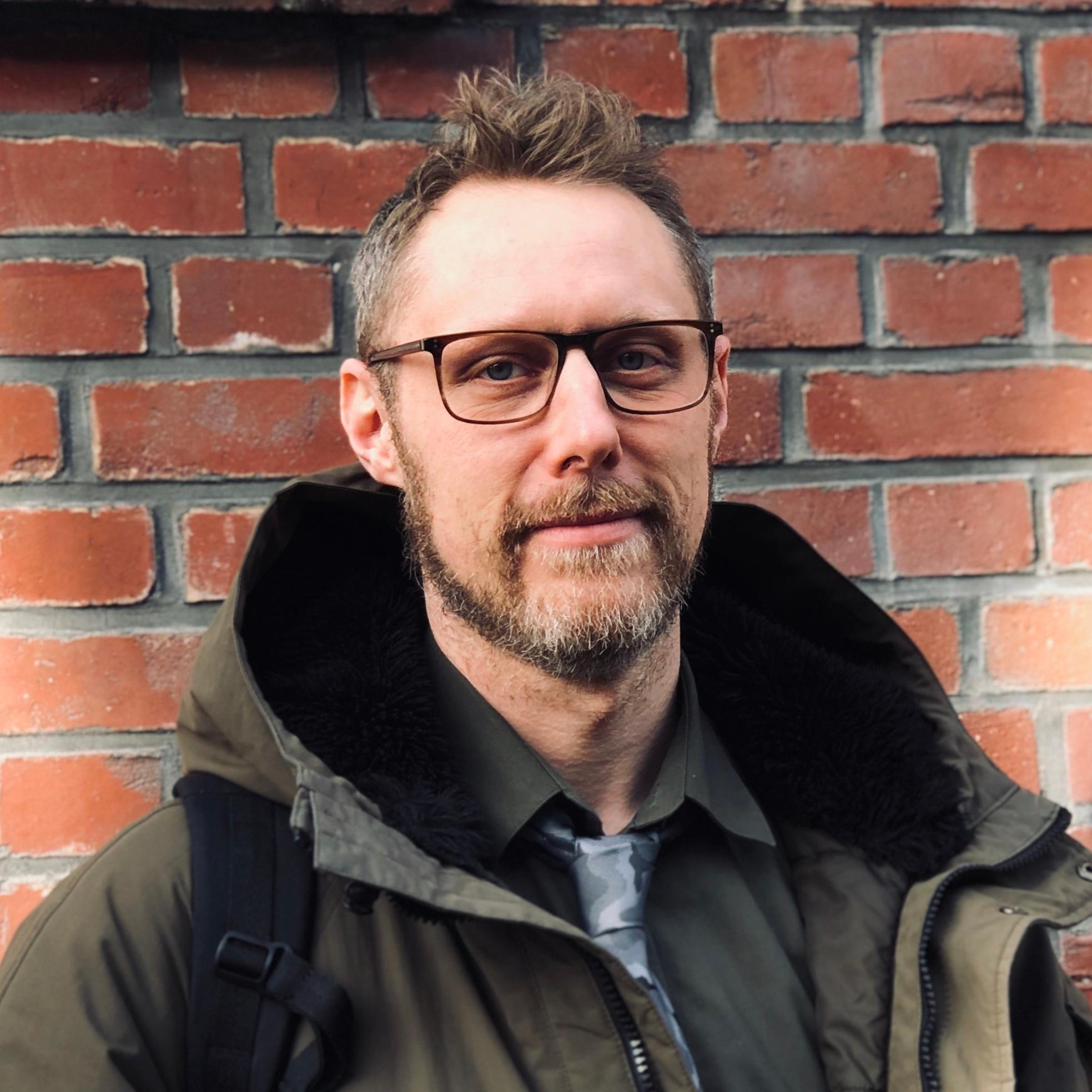 Porträt eines Mannes mit Brille vor einer Backsteinmauer