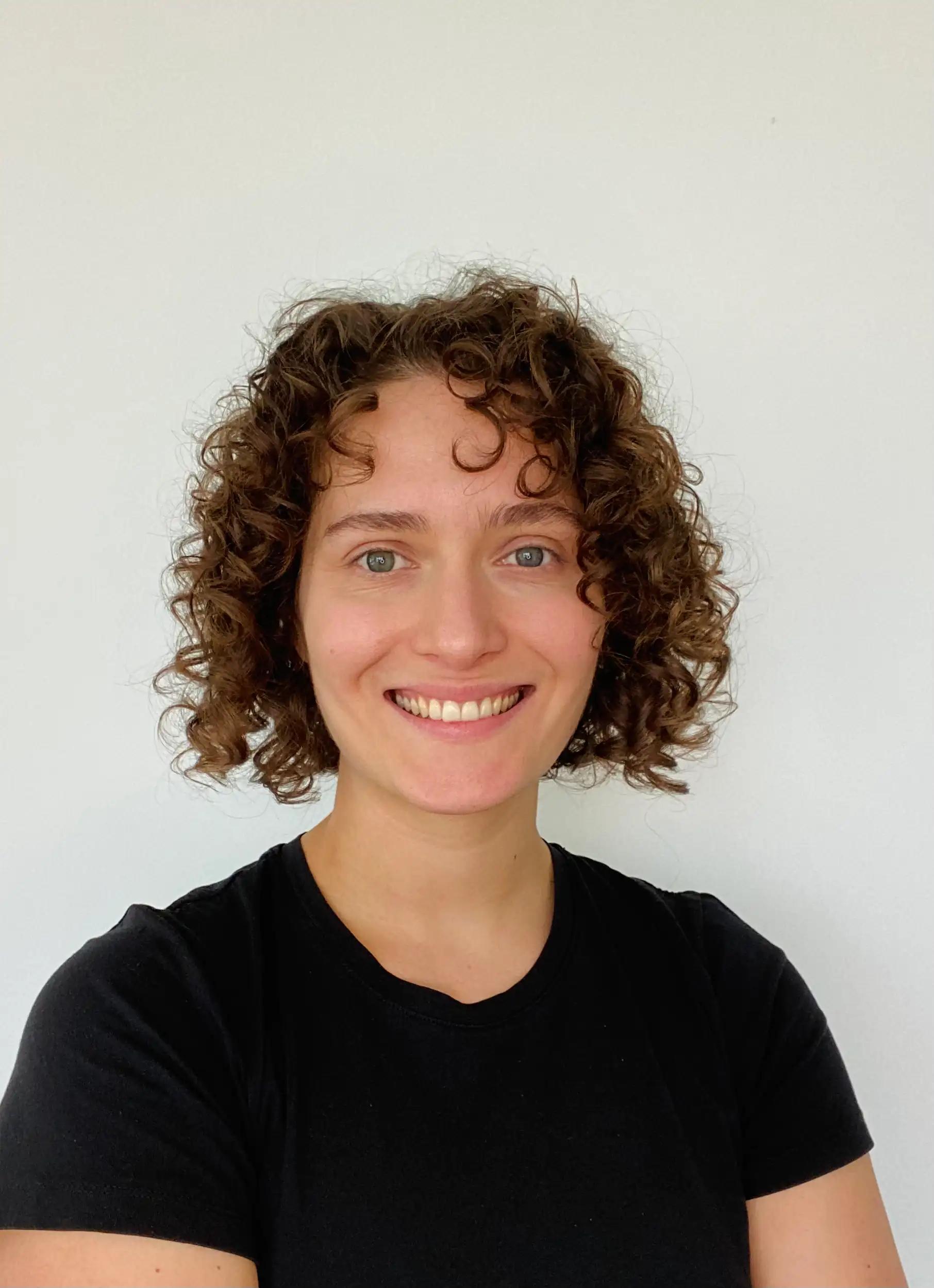 Porträt einer lächelnden Frau mit lockigem Haar vor weißem Hintergrund