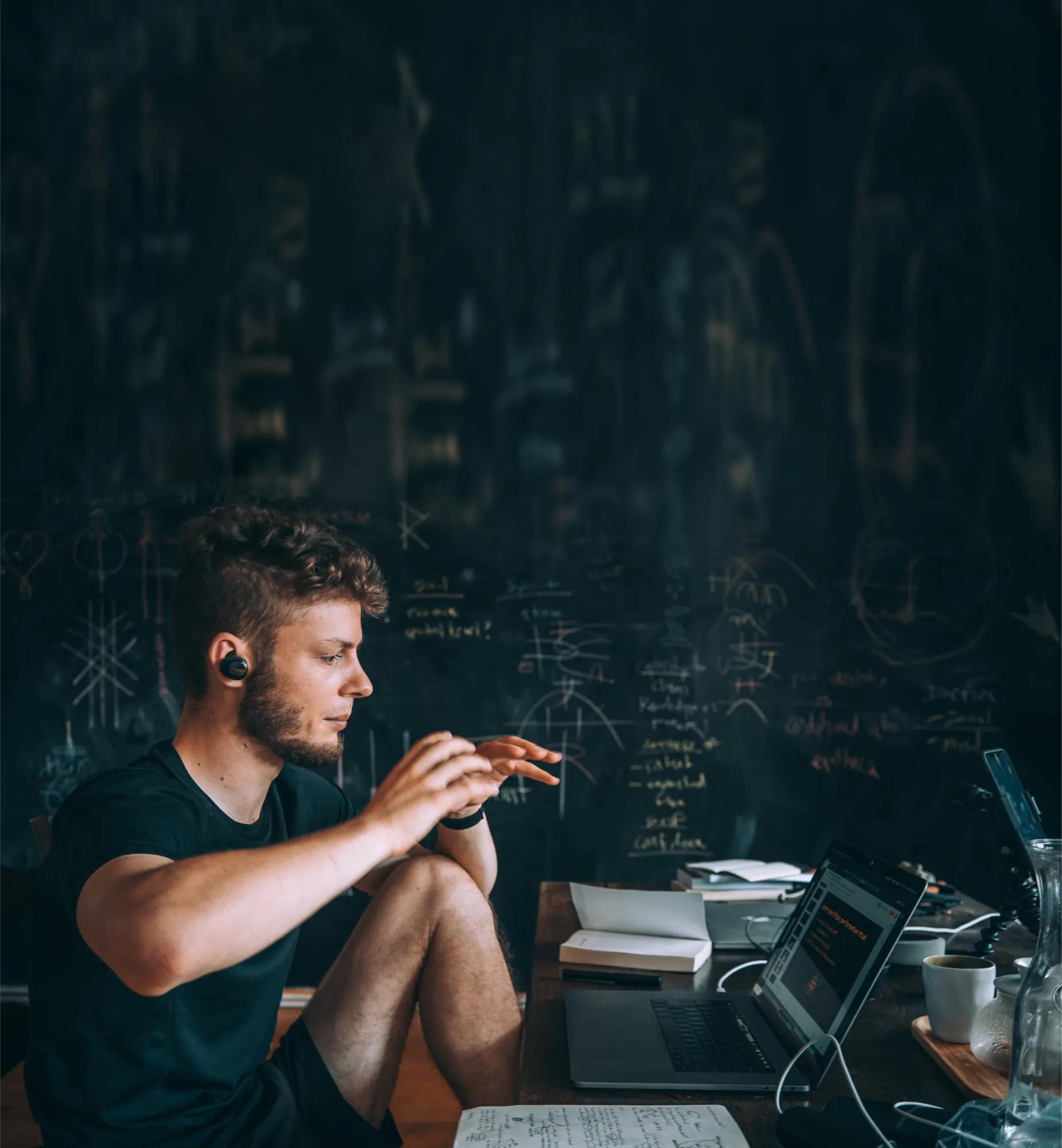 Mann arbeitet mit Laptop und Notizen in einem dunklen Raum.